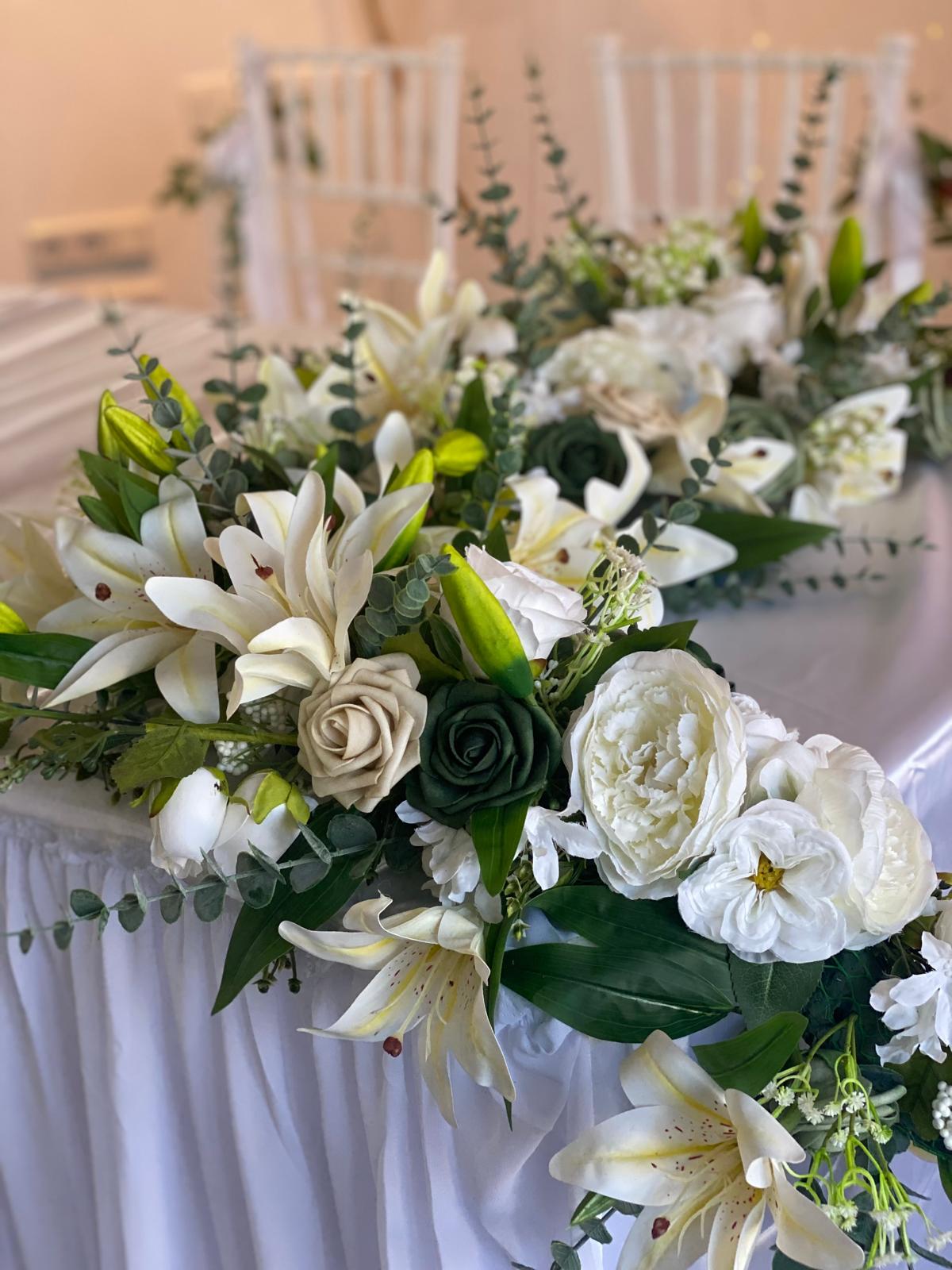 Elegante Blumenarrangements mit weißen Lilien und Rosen auf festlich gedecktem Tisch